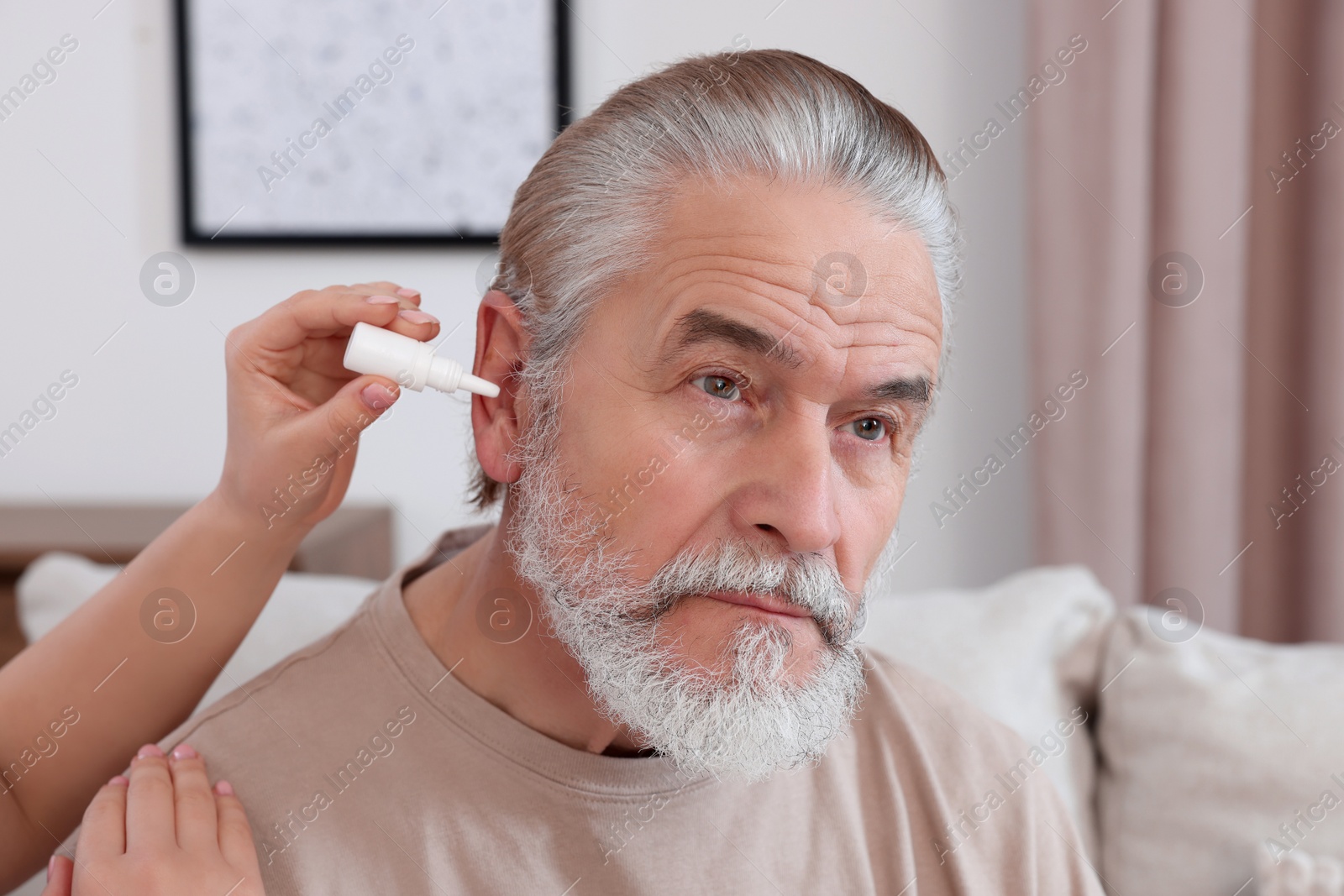 Photo of Young woman dripping medication into man's ear at home