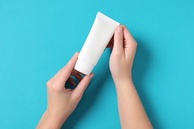 Woman with tube of hand cream on light blue background, top view