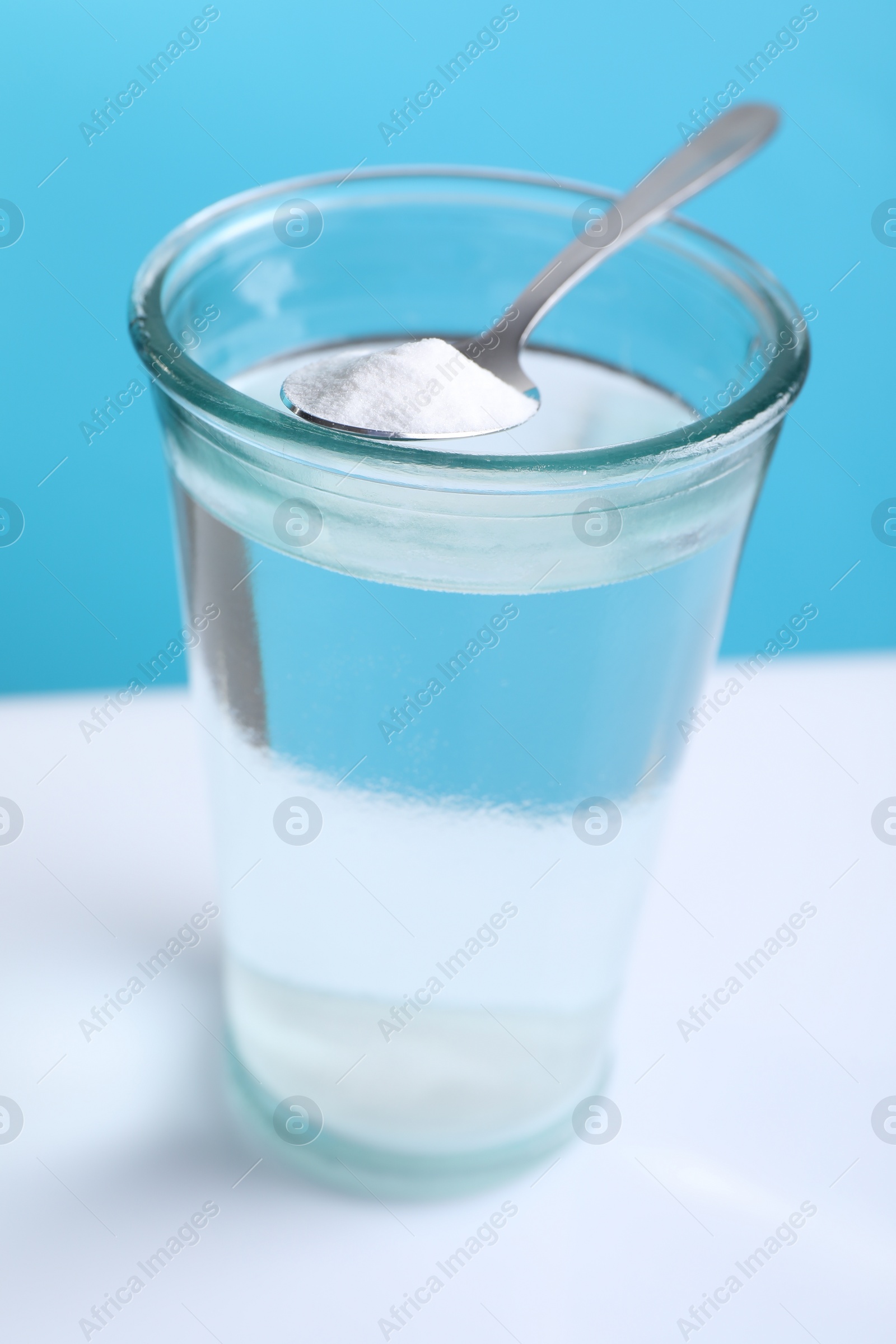 Photo of Glass of water and spoon with baking soda on color background, closeup