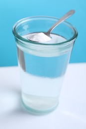 Glass of water and spoon with baking soda on color background, closeup