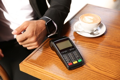Photo of Man making payment with smart watch in cafe, closeup