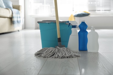 Photo of Bucket, mop and different cleaning products on floor indoors