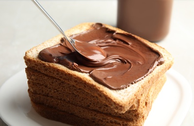 Photo of Spreading sweet chocolate cream onto toast on table, closeup