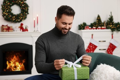 Happy young man opening Christmas gift at home