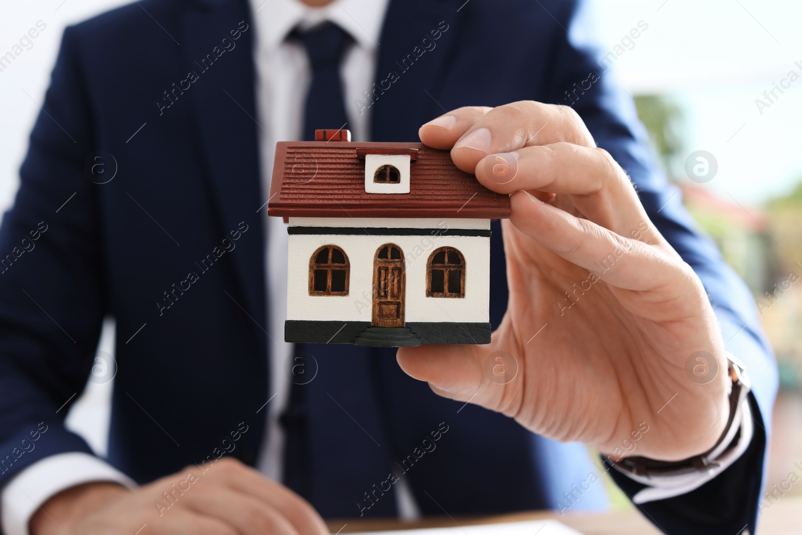 Photo of Real estate agent holding house model at table in office, closeup