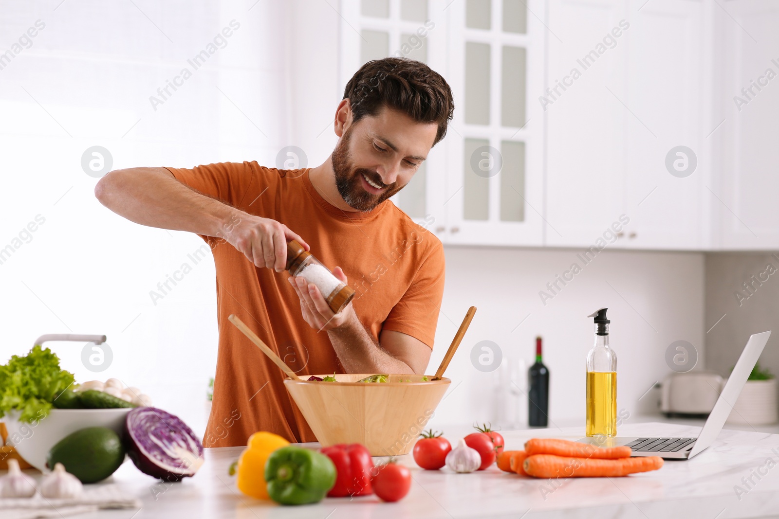 Photo of Man making dinner while watching online cooking course via laptop in kitchen