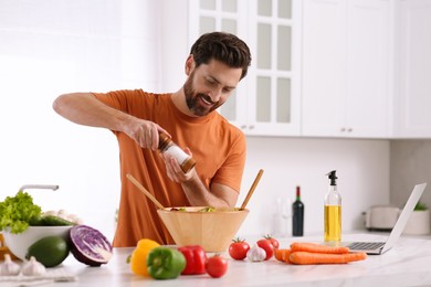 Man making dinner while watching online cooking course via laptop in kitchen