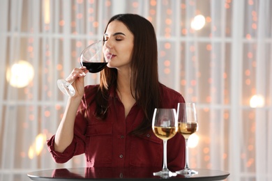 Beautiful young woman tasting luxury wine at table indoors