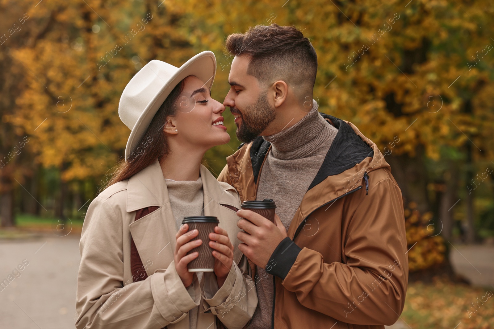 Photo of Happy young couple with cups of coffee spending time together in autumn park