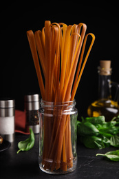 Photo of Uncooked buckwheat noodles and fresh ingredients on black table