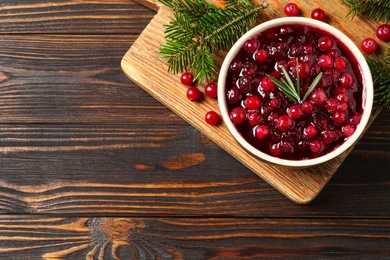 Photo of Cranberry sauce, and fir tree branches on wooden table, top view. Space for text