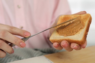 Woman spreading tasty nut butter onto toast at table, closeup