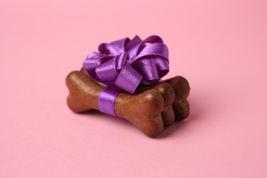 Photo of Bone shaped dog cookies with purple bow on pink background, closeup