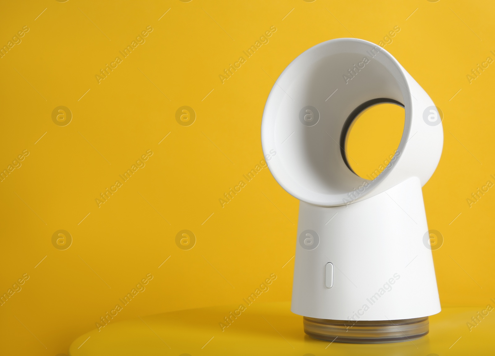 Photo of Modern electric fan on yellow table. Space for text