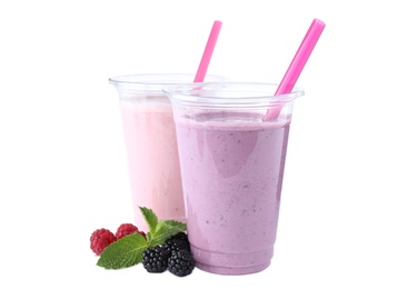 Photo of Tasty fresh milk shakes in plastic cups with ingredients on white background