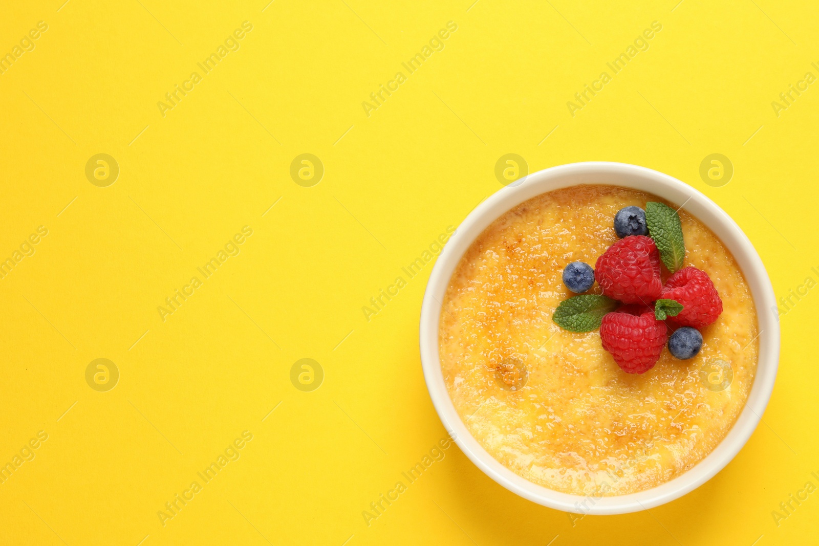 Photo of Delicious creme brulee with fresh berries and mint on yellow background, top view. Space for text