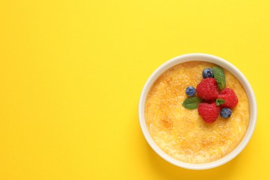Photo of Delicious creme brulee with fresh berries and mint on yellow background, top view. Space for text