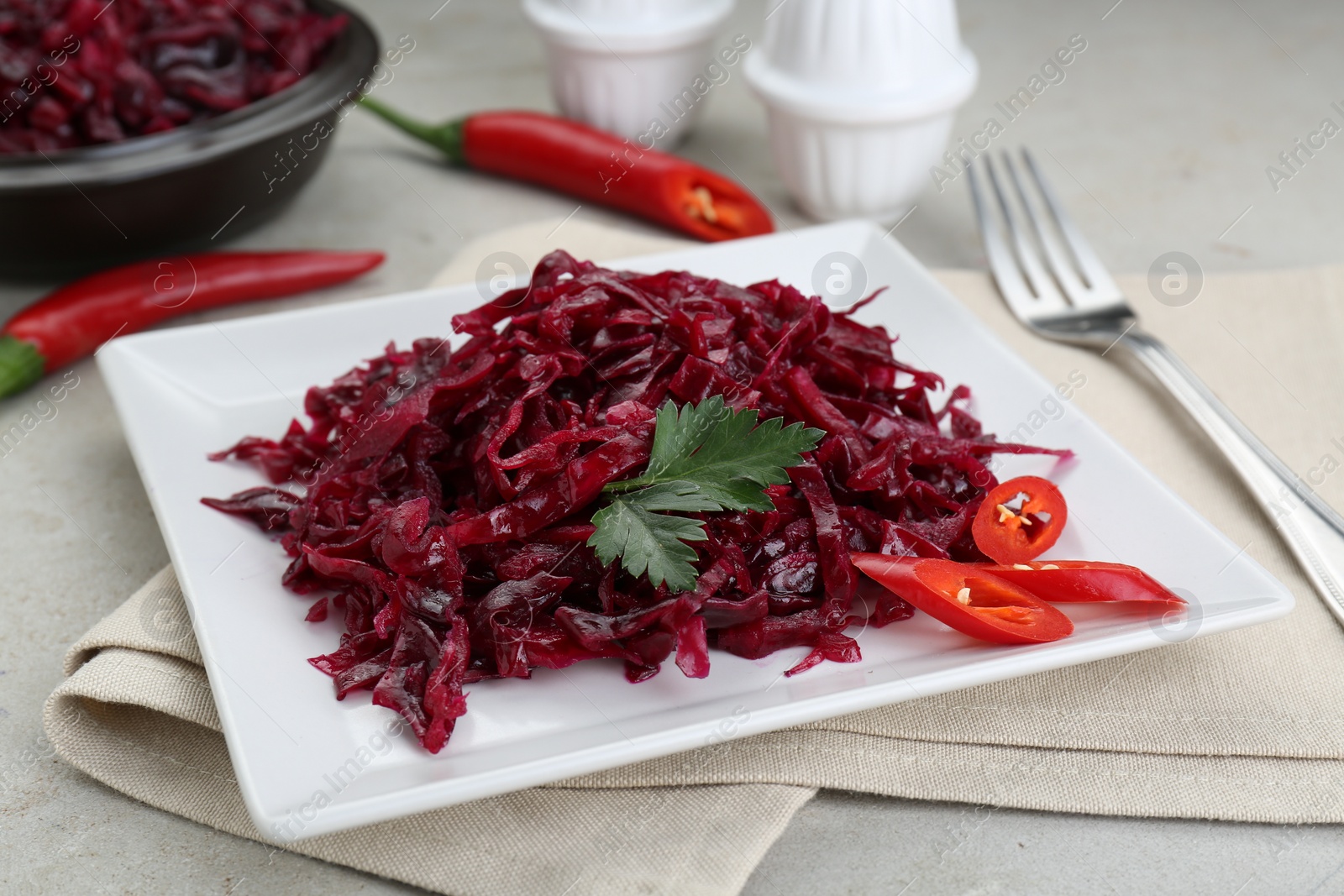 Photo of Tasty red cabbage sauerkraut with chili pepper and parsley served on light table