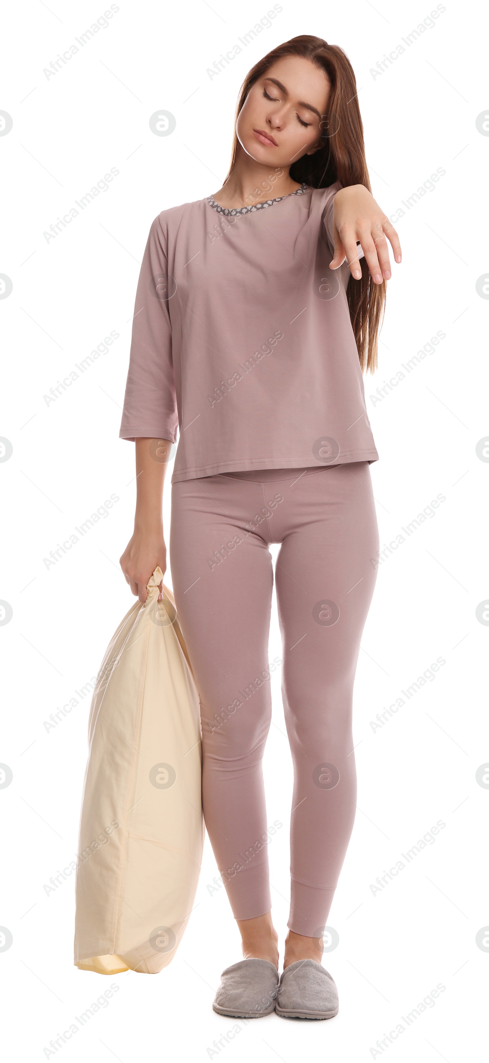 Photo of Young woman wearing pajamas and slippers with pillow in sleepwalking state on white background