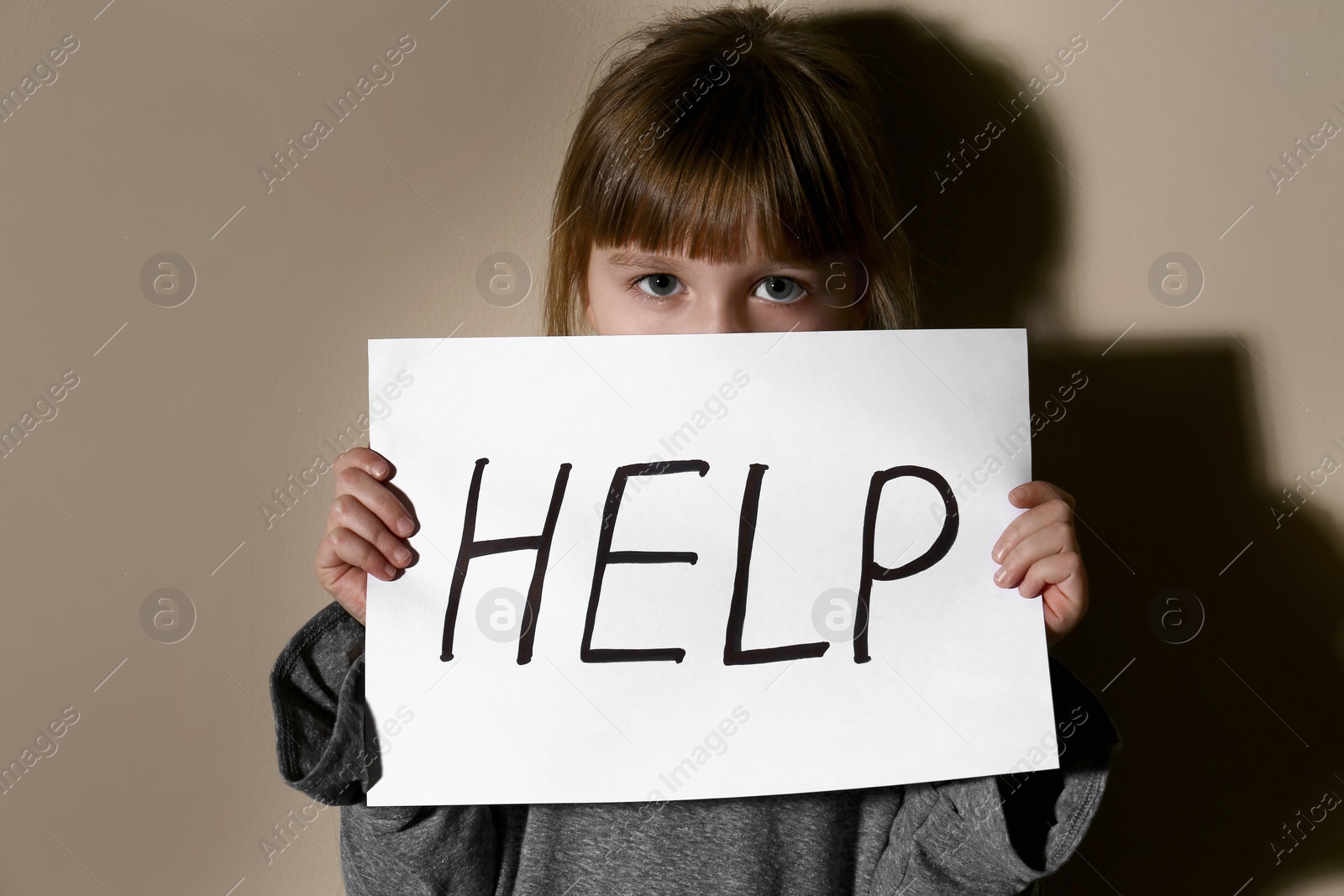 Photo of Abused little girl with sign HELP near beige wall. Domestic violence concept