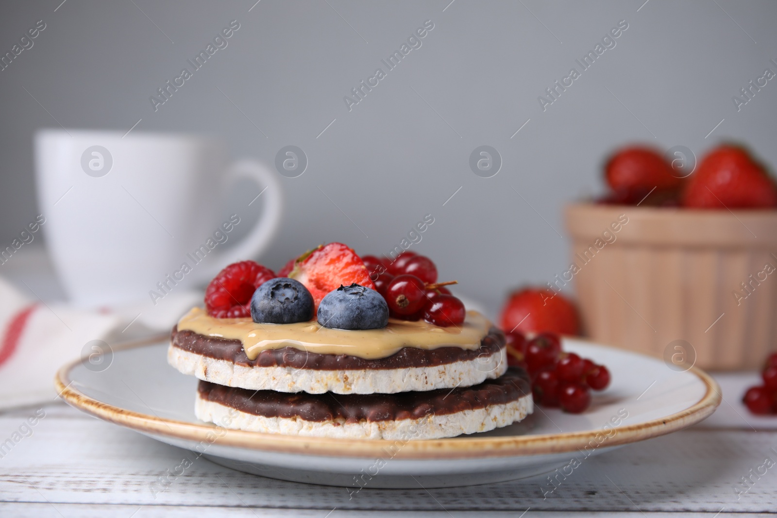 Photo of Crunchy rice cakes with peanut butter and sweet berries served on white wooden table, closeup