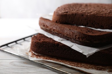 Photo of Layers of homemade chocolate sponge cake on white wooden table, closeup