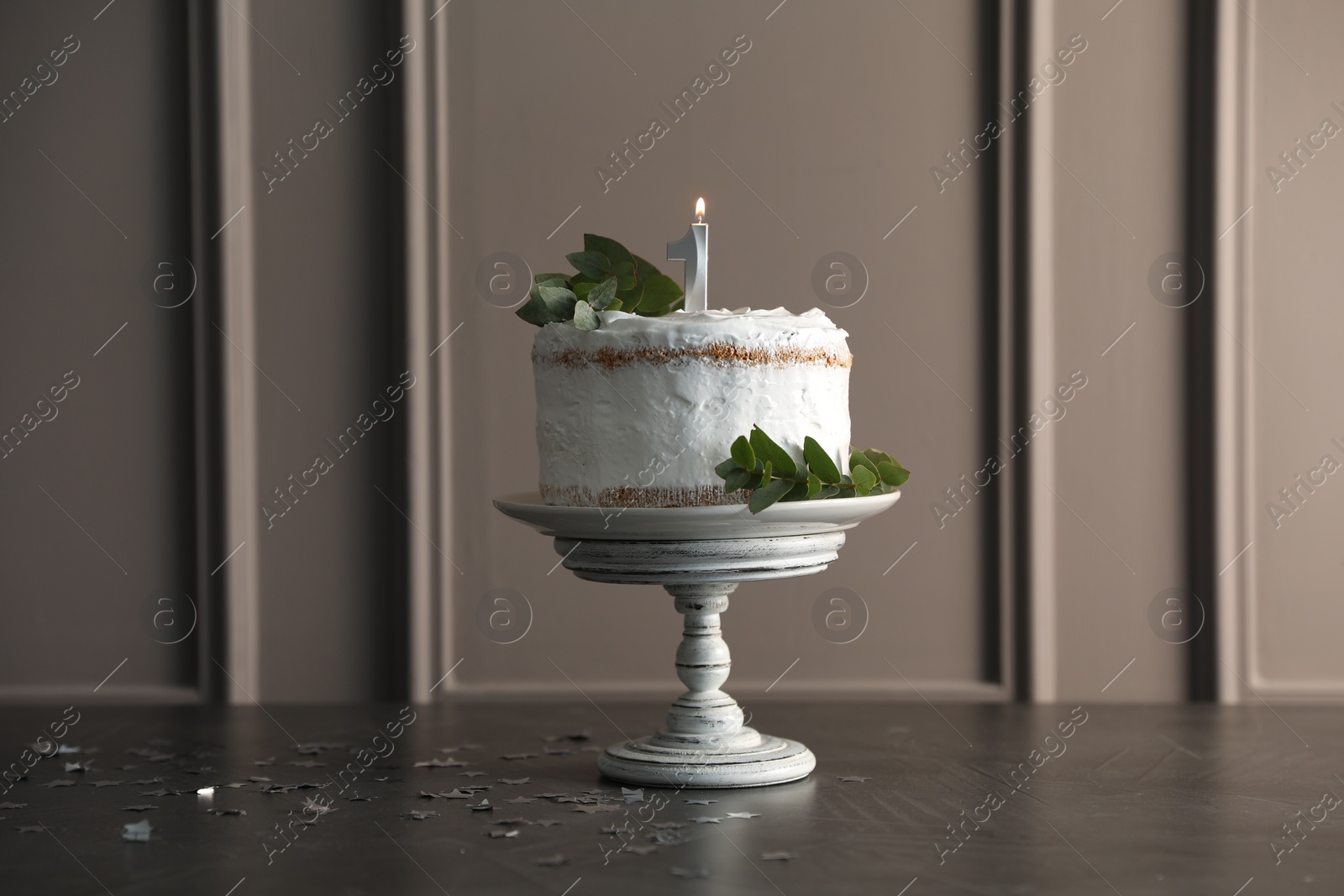 Photo of Tasty Birthday cake with burning candle and eucalyptus branches on grey table