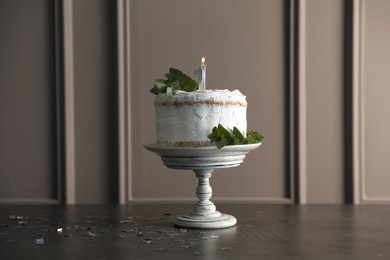 Photo of Tasty Birthday cake with burning candle and eucalyptus branches on grey table