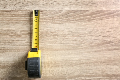 Photo of Metal measuring tape on wooden background, top view. Space for text