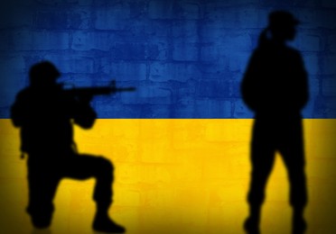 Silhouettes of soldiers and brick wall painted in Ukrainian flag colors on background, space for text. Military service during war