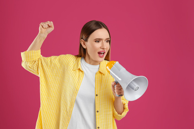 Emotional young woman with megaphone on pink background