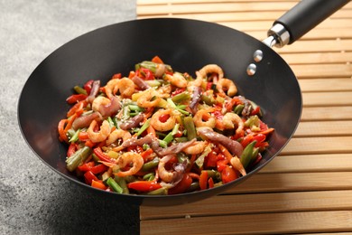 Photo of Shrimp stir fry with vegetables in wok on grey table