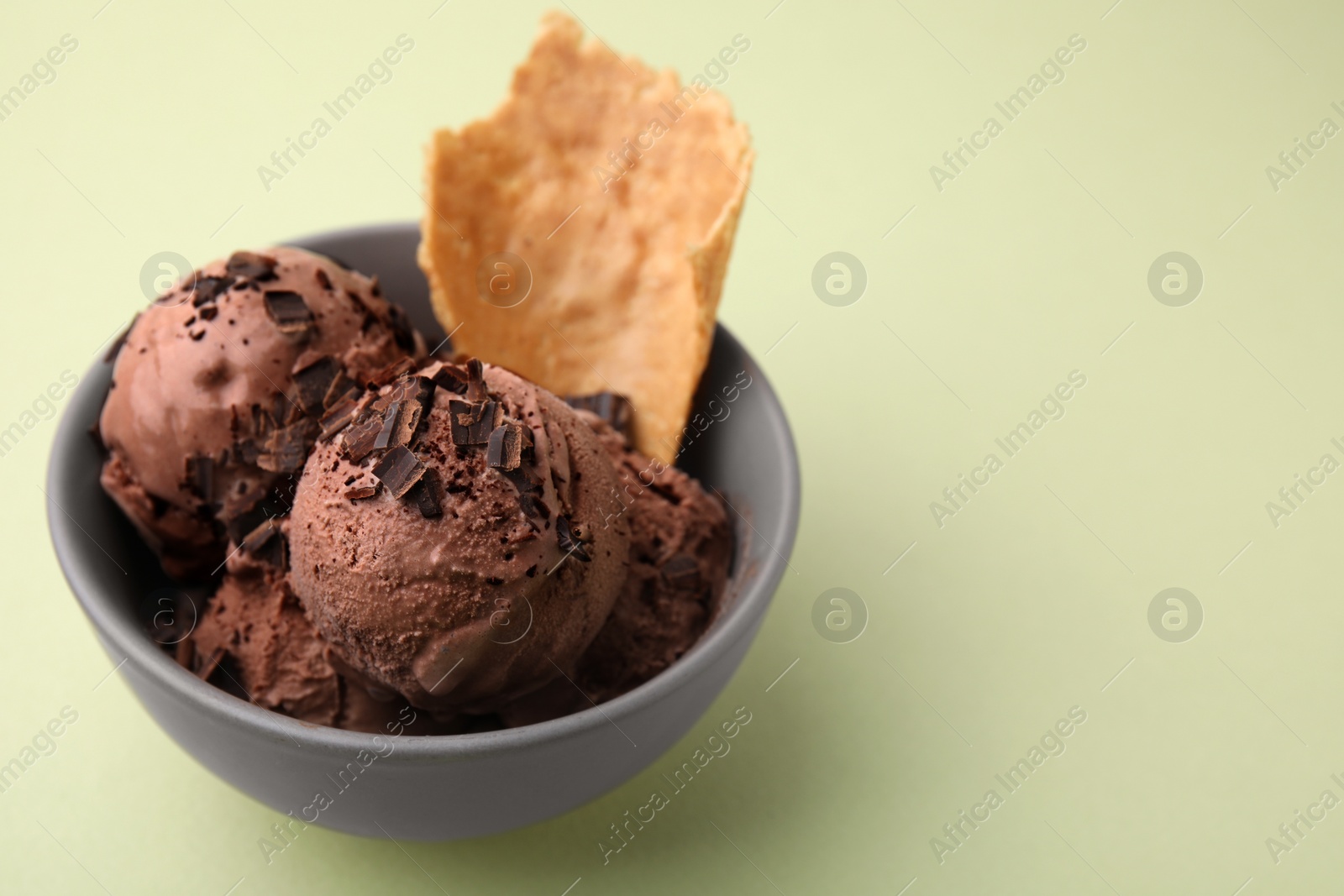 Photo of Tasty chocolate ice cream and piece of waffle cone in bowl on light green background, closeup. Space for text