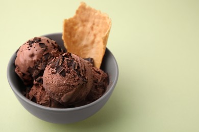 Tasty chocolate ice cream and piece of waffle cone in bowl on light green background, closeup. Space for text