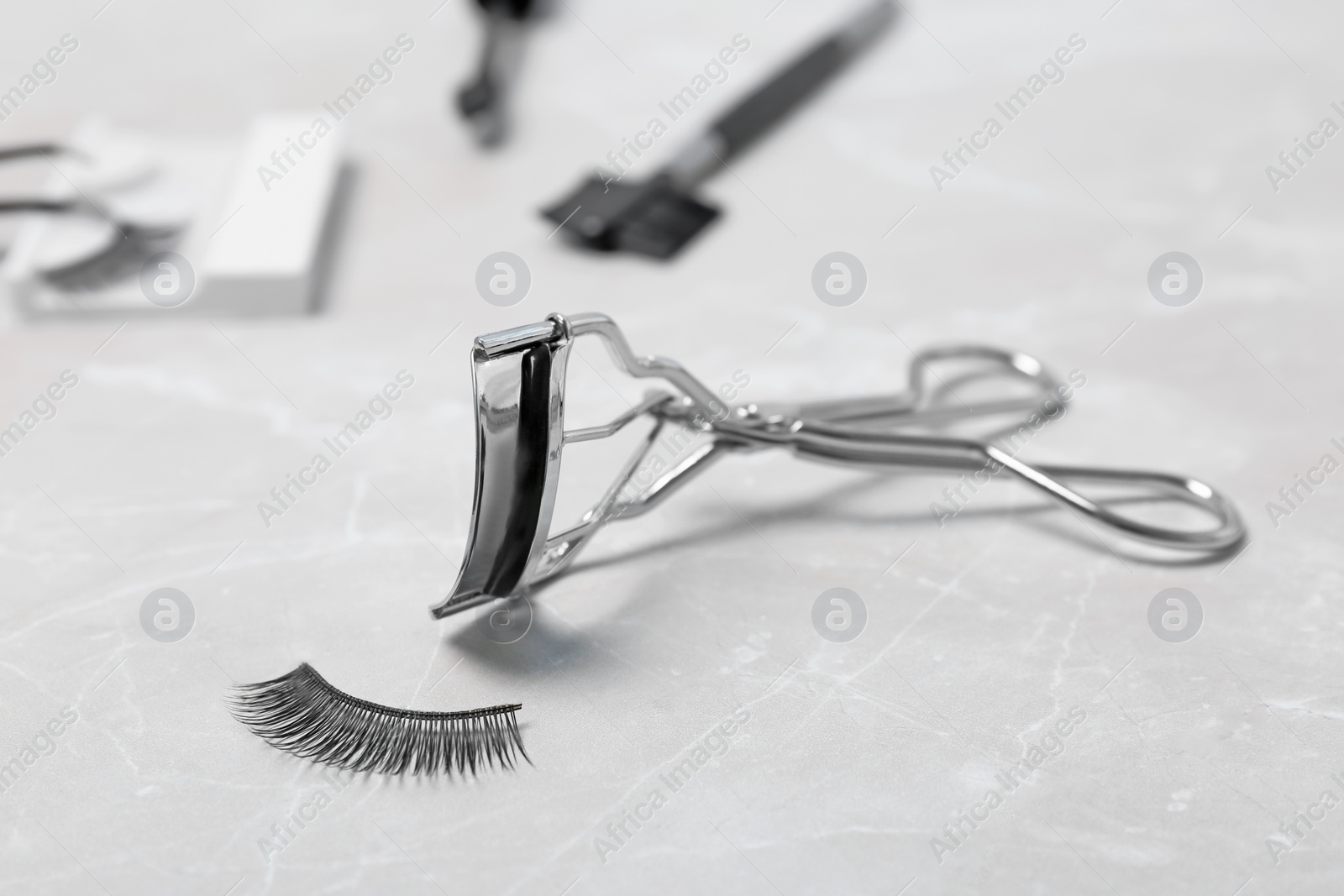 Photo of Curler and false eyelashes on grey background, closeup