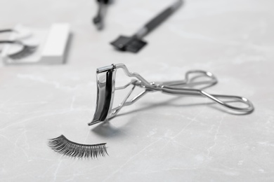 Curler and false eyelashes on grey background, closeup