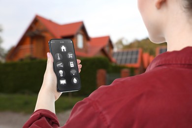 Image of Woman using smart home control system via mobile phone near house outdoors, closeup