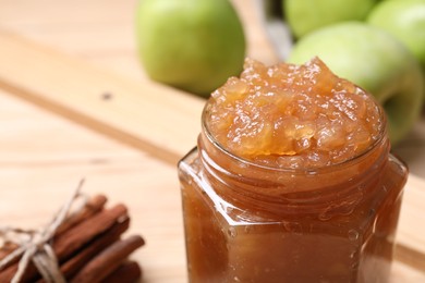 Delicious apple jam in jar, fresh fruits and cinnamon on table, closeup. Space for text