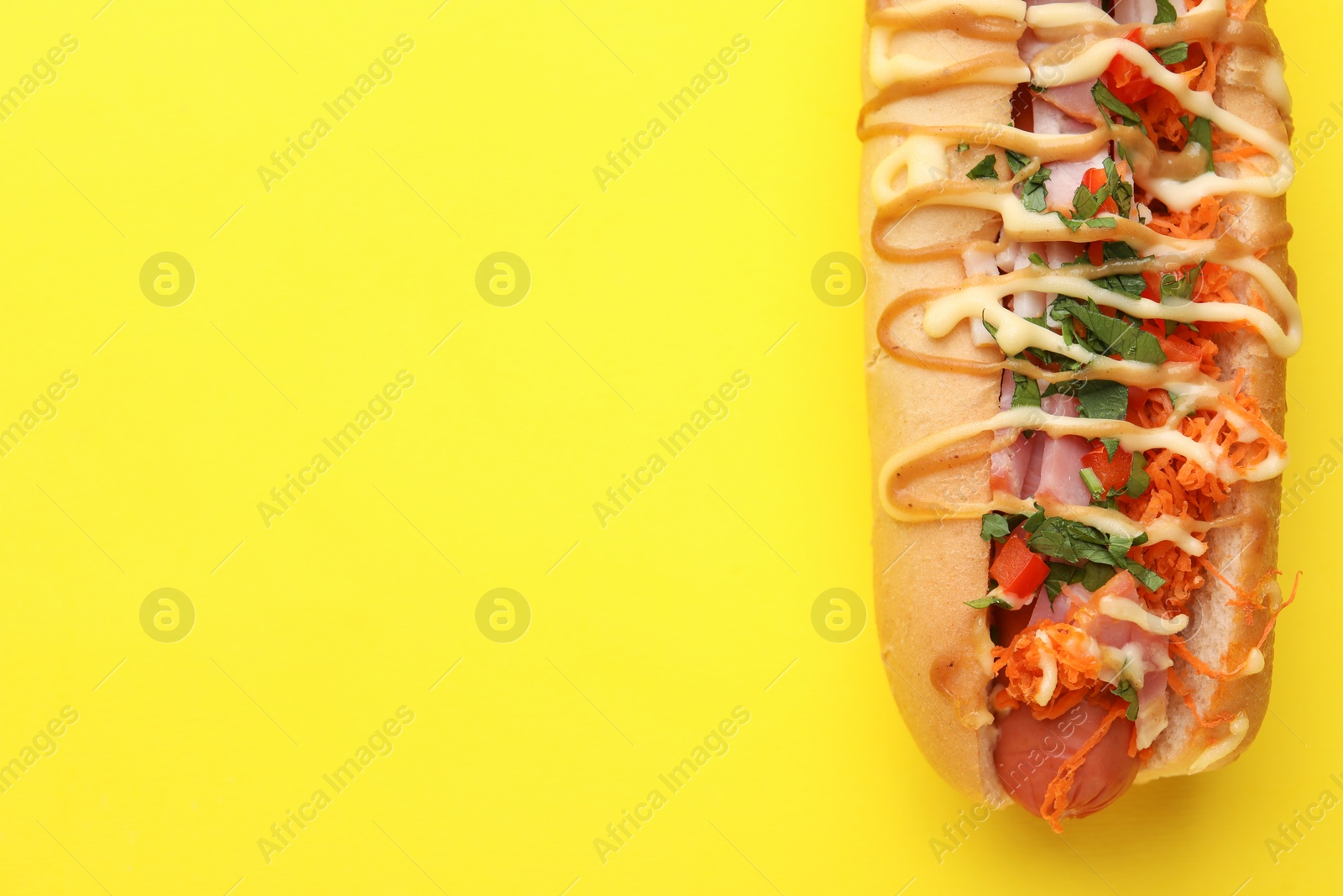 Photo of Delicious hot dog with bacon, carrot and parsley on yellow background, top view. Space for text