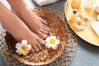 Closeup view of woman soaking her feet in dish with water and flowers on grey floor. Spa treatment