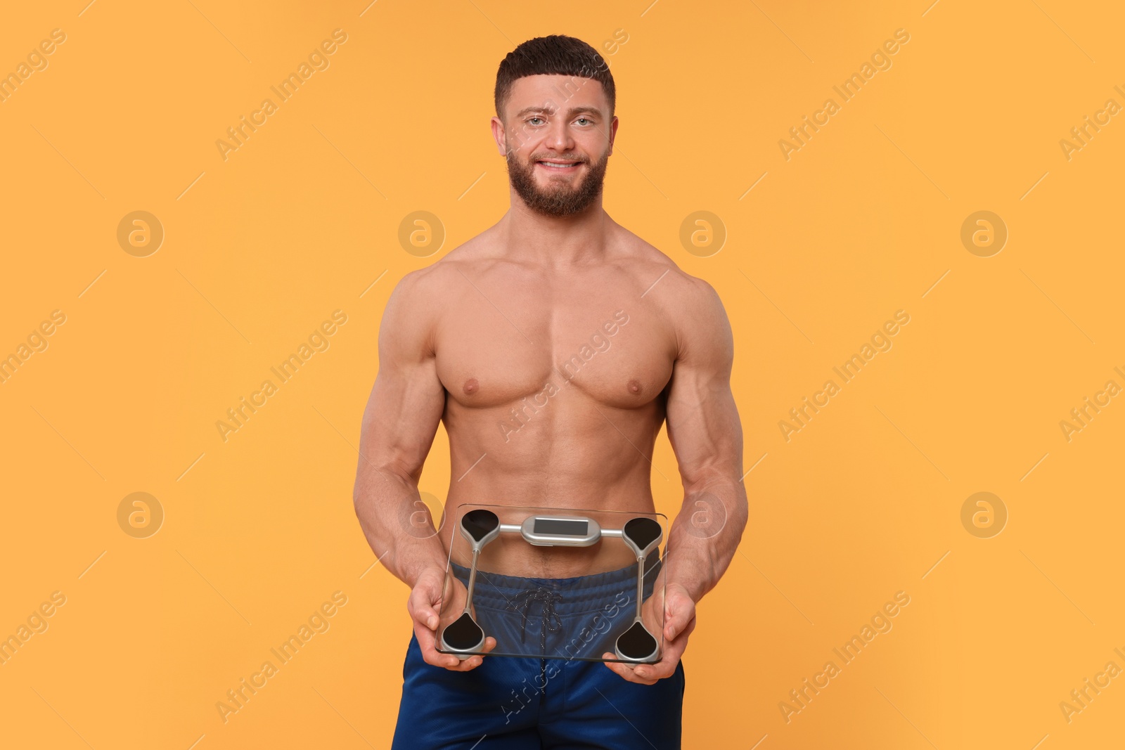 Photo of Portrait of happy athletic man with scales on orange background. Weight loss concept