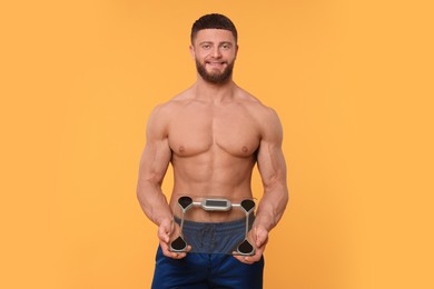 Photo of Portraithappy athletic man with scales on orange background. Weight loss concept