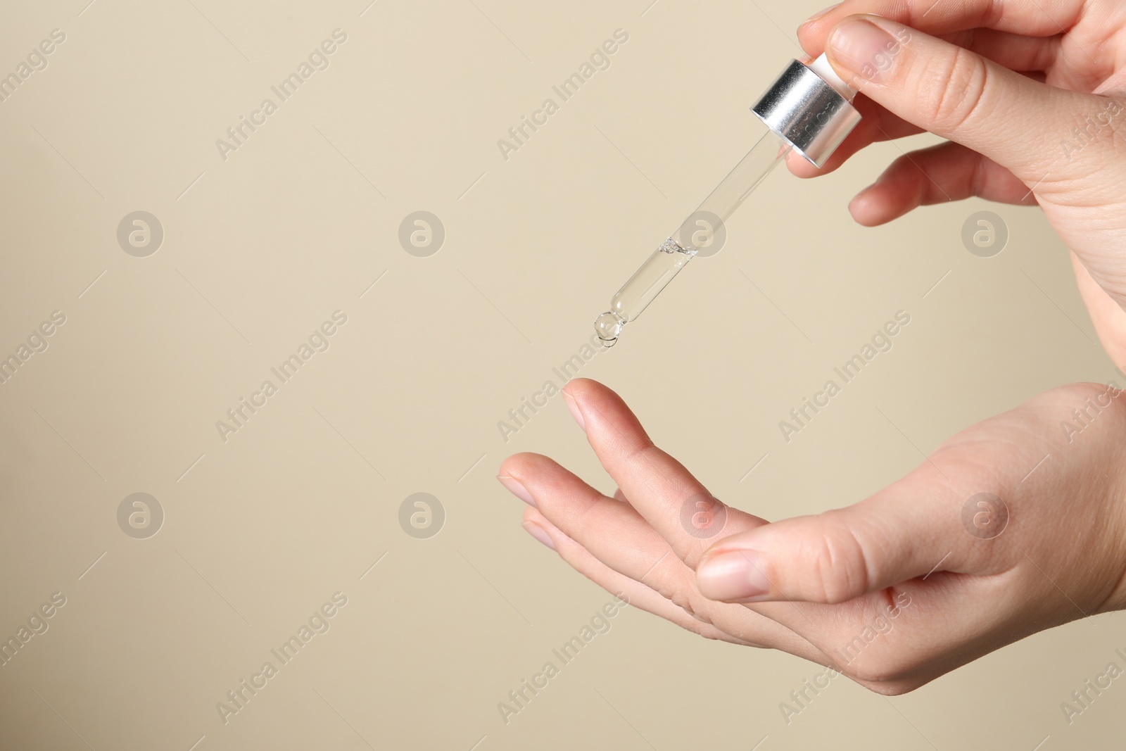 Photo of Woman applying cosmetic serum onto finger on beige background, closeup. Space for text