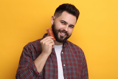 Handsome young man combing beard on yellow background