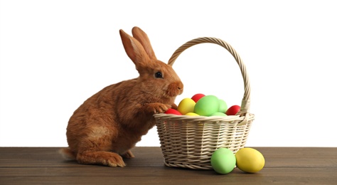 Cute bunny and basket with Easter eggs on wooden table against white background