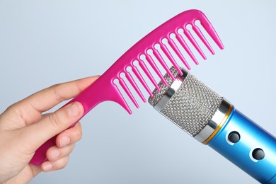 Photo of Woman making ASMR sounds with microphone and comb on grey background, closeup