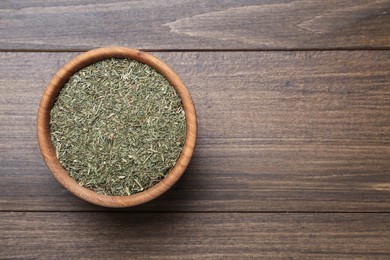 Photo of Bowl of dried dill on wooden table, top view. Space for text