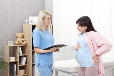 Photo of Doctor with clipboard consulting pregnant patient in clinic