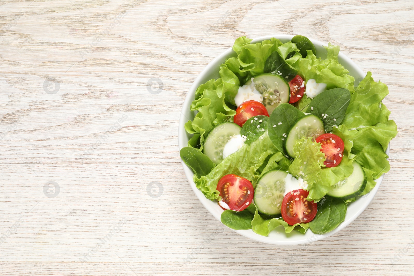 Photo of Delicious salad in bowl on white wooden table, top view. Space for text