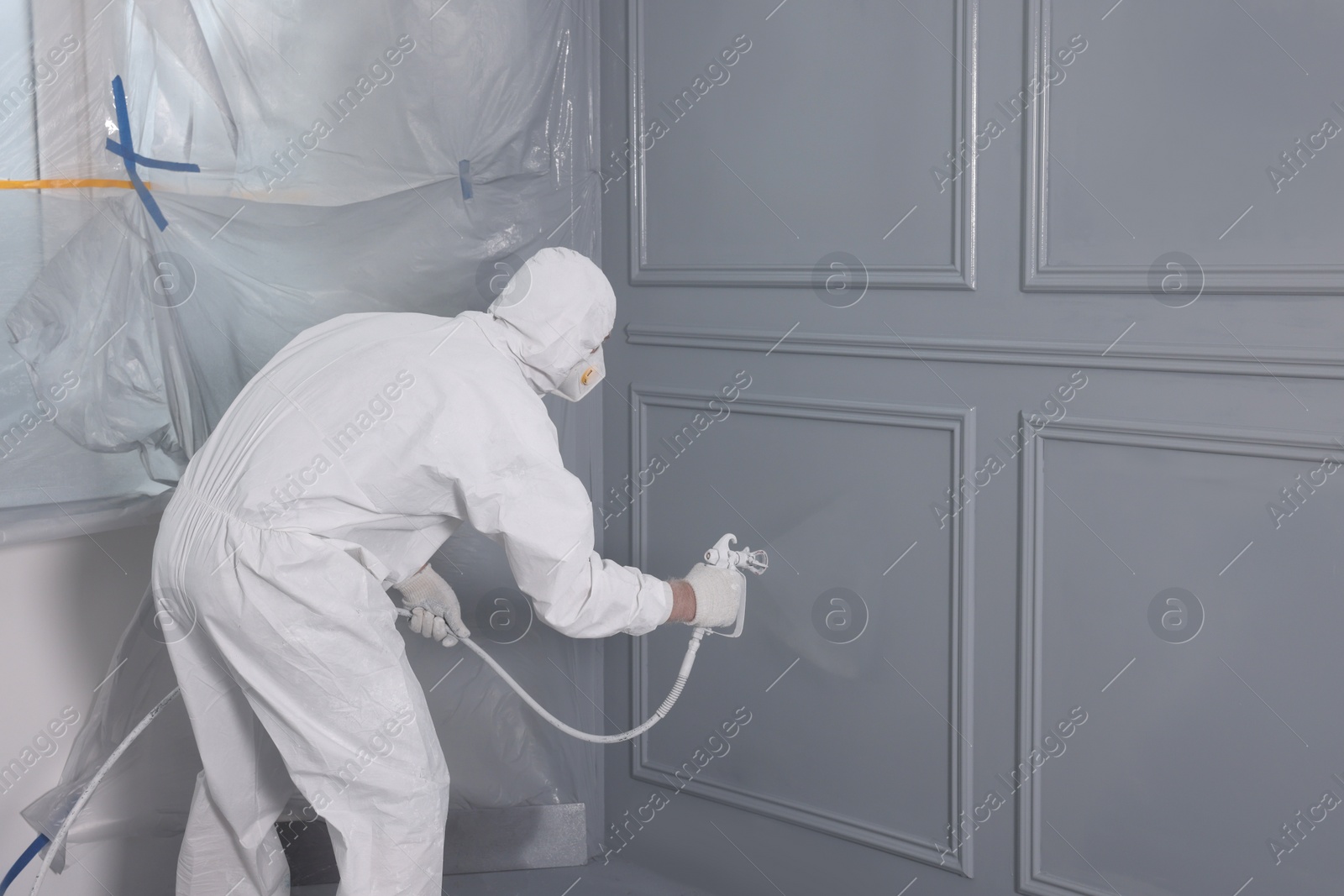 Photo of Decorator dyeing wall in grey color with spray paint, back view